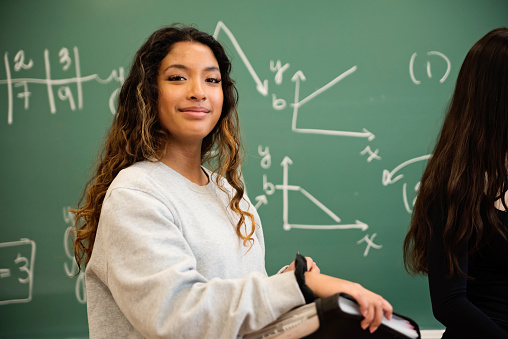 Long hair young asian female college student portrait in front of a chalkboard with mathematical formula. This is part of a series promoting diversity and equity in STEM. Horizontal waist up indoors shot with copy space. This was taken in Montreal, Quebec, Canada.