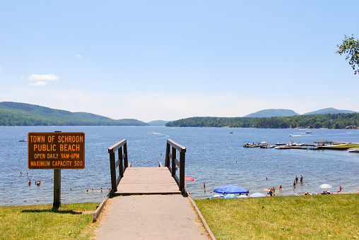 Summertime at Schroon Lake Beach in the Adirondacks, New York State showing sign, path, and steps down to beach with lake.