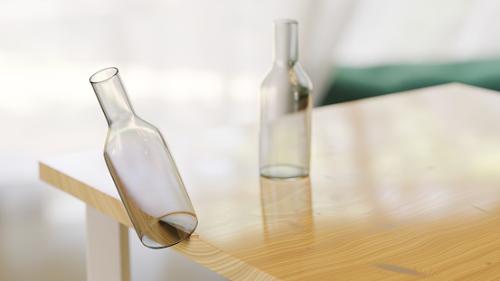 Two glass bottles are on a table; one of them is on the edge and about to fall. CGI!