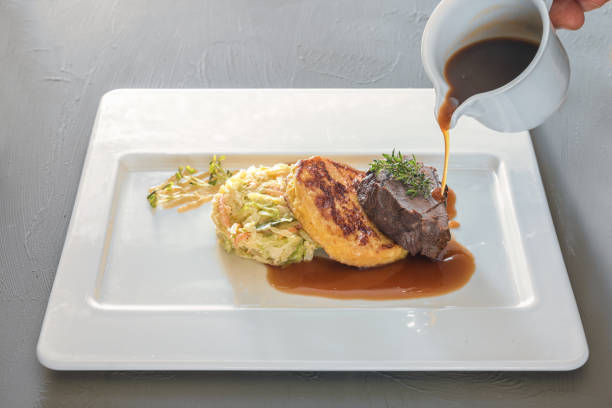 istock Pouring sauce on a dish from roast venison, flat bread dumpling and round shaped cabbage vegetable on a white plate, preparation for delicious gourmet meal, copy space 1483945328