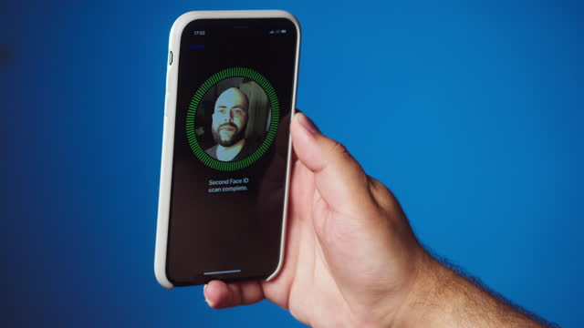 Man scanning face id on phone close-up. Male person using smartphone unlocking with biometric facial identification on blue background. Facial recognition.