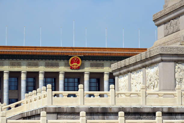 Great Hall of the People - parliament and meeting hall, Beijing, China Beijing, China: Great Hall of the People façade with Chinese coat of arms, seen behind the Monument to the People's Heroes. One of the most symbolic buildings in Beijing. The neoclassical-style building designed by Zhang Bo is located on the west side of Tiananmen Square and serves the Chinese leadership as a place to receive state guests and as a venue for national celebrations and as the meeting place of the Chinese parliament (National People's Congress). tiananmen square stock pictures, royalty-free photos & images