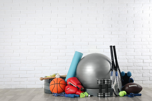 Set of different sports equipment on floor near white brick wall