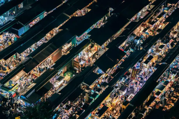 A drone captures time-lapse footage of Taiwan's bustling night markets. The crowds weave through stalls and sample street food, while neon lights and bright signs illuminate the scene. The lively atmosphere captures the essence of the Asian lifestyle, as locals and tourists alike enjoy the night markets as a destination for both shopping and nightlife. From the colorful lanterns to the steam rising from sizzling snacks, the drone's aerial perspective captures the unique energy and excitement of Taiwan's bustling night markets.