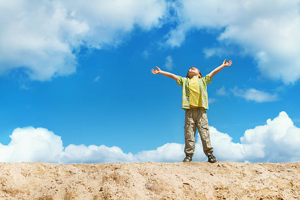 Happy child standing with hands raised up over blue sky