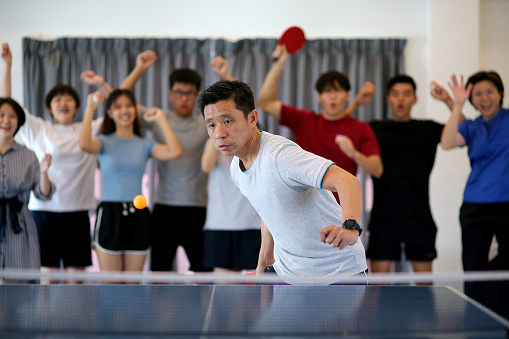 View of an orange table tennis ball in motion. Blue tennis table on a background. Copy space.