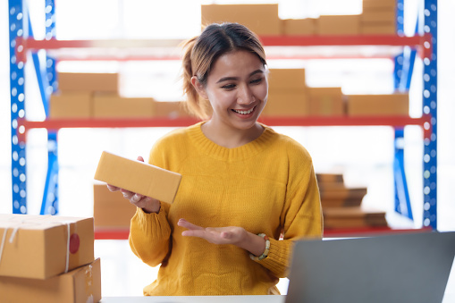 Asian business owner prepare boxed product to send to customer and have online video calls with them.