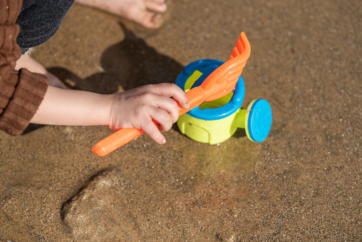 A little girl's hand holding a toy on the beach is playing sand on the beach