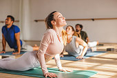An Attractive Female With Closed Eyes Doing A Cobra Pose During A Yoga Class In A Beautiful Studio With Natural Sunlight