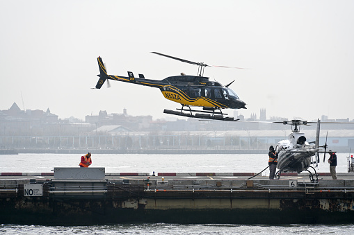 A taxi helicopter sits poised for takeoff at a bustling terminal in New York City's financial district, offering premium helicopter charter services amid the iconic Manhattan skyline.