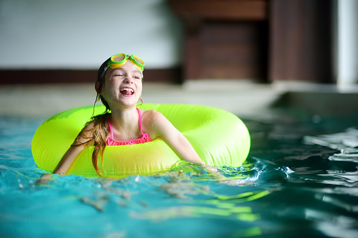 Cute little girl playing with inflatable ring in indoor pool. Child learning to swim. Kid having fun with water toys. Family fun in a pool.