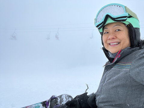 Chinese woman in 60s taking a selfie while snowboarding.  North Vancouver, British Columbia, Canada.