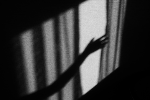 Shadow of a hand reaching for the curtain