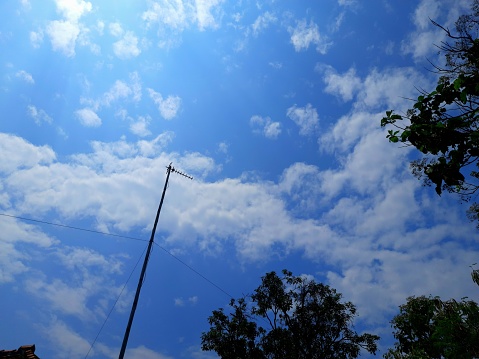 tv antenna mast with a background of blue sky and shady trees