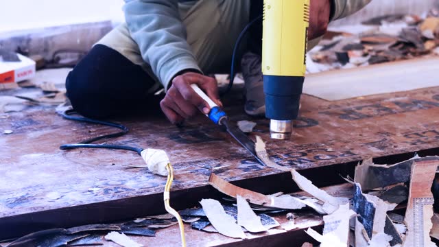 Carpenter removing old varnish from wood using scraper and heat gun