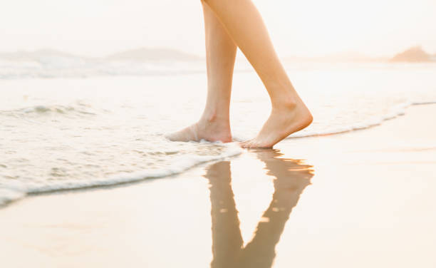Woman's legs stand on the beach at sunset time.