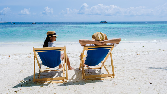 a couple of men and women on beach chairs on the beach of Koh Lipe Island Southern Thailand, with turqouse colored ocean and white sandy beach at Ko Lipe.