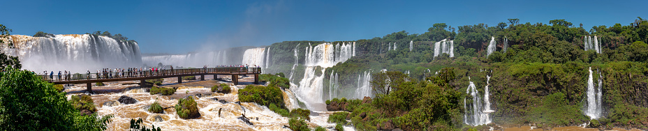 Panorama of spectacular Iguazu Falls with visitor platform and blue sky