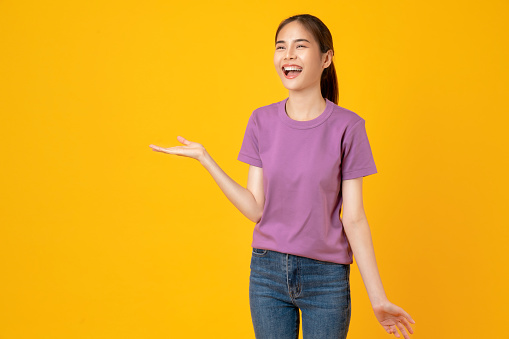 Happy smiling young woman wearing casual purple t-shirt with shows hand to the side, isolated on yellow background.