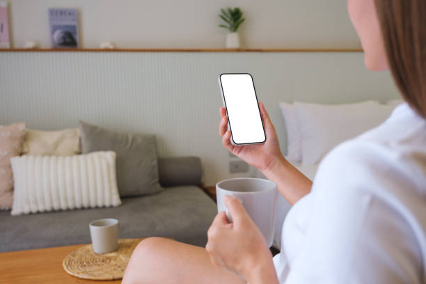 istock Mockup image of a woman holding and using mobile phone with blank desktop white screen while drinking coffee at home 1484023409