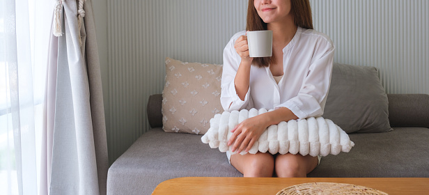 Closeup image of a beautiful woman drinking hot coffee and relaxing on a sofa at home