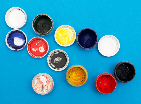 Watercolor paints or poster paints in mini cans and paintbrushes isolated on white.