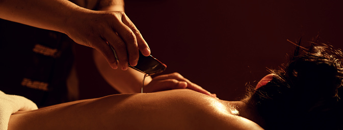 Masseur pouring aroma oil on back woman customer in cosmetology spa centre. Aromatherapy massage,