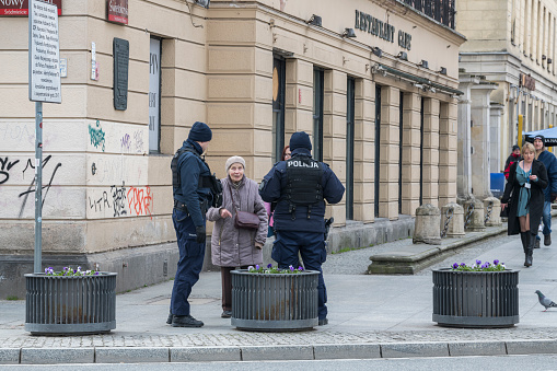 Older womand talking to two policeman in the street with pedestrians in the background. 5 april 2023, Warsaw, Poland.