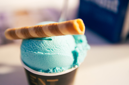 a ball of ice cream in a paper cup on top with a tube of sweet, a close-up on the ice cream that stands on the table there is a place for an inscription