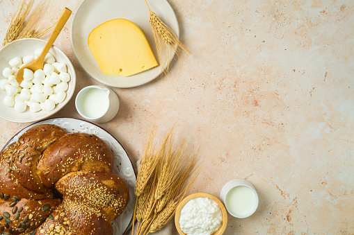Jewish holiday Shavuot concept with challah bread, milk and cheese on stone table background. Top view from above