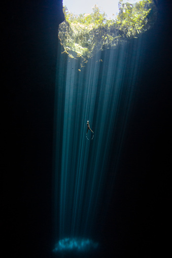 Japanese Freediver gracefully surfacing under a Mayan Cenote