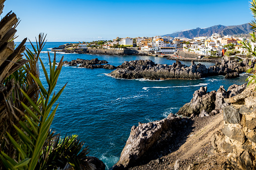 Panoramic view of the idyllic Tenerife fishing village of Alcalá, framed by a rocky coastline with Playa de Alcalá beach at the Atlantic Ocean and the Montana de Guama mountain in the background.