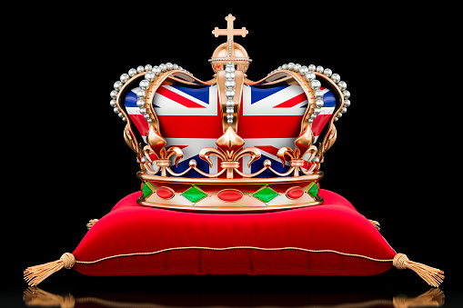 Royal golden crown with the United Kingdom flag on red vilvet pillow on dark background