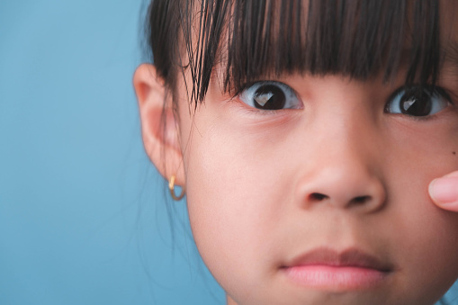 Close-up portrait of surprised young Asian girl isolated on blue background. Cute shocked young girl with big black eyes reacts surprisingly to something, looking at the camera. negative mood child