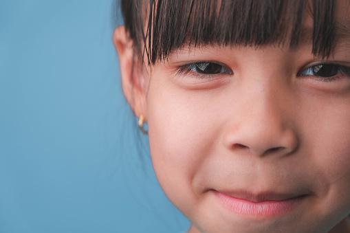 Portrait of a smiling little girl looking at the camera. Close up of cute Asian girl face posing on blue background.