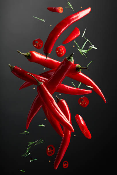 Falling red chili peppers and rosemary on a black background. stock photo