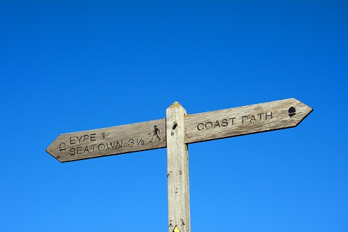 Wooden coast path sign with walking route to Eype and Seaton against a blue sky, West Bay, Dorset, UK, Europe
