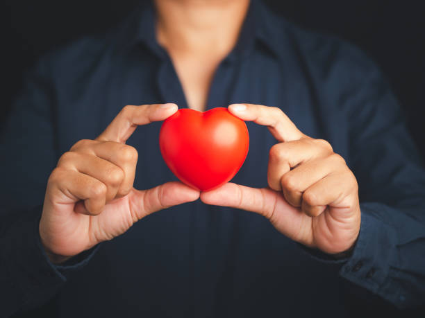 istock A young man in a blue shirt holding a red heart shape while standing on a black background. 1484055698