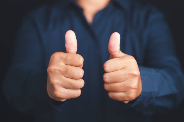 istock Midsection of businessman showing thumbs up while standing on a black background. 1484055808