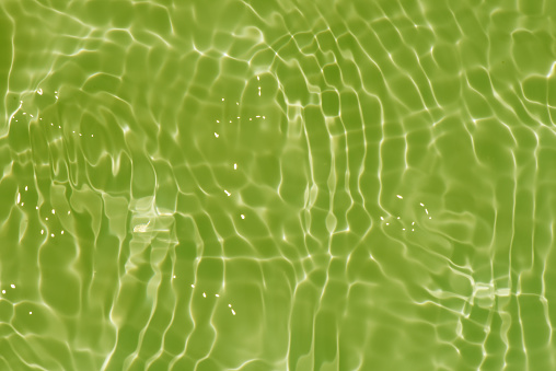 Light green water with ripples on the surface. Defocus blurred transparent colored clear calm water surface texture with splashes and bubbles. Water waves with shining pattern texture background.