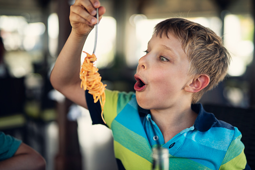 Happy little boy aged 7 is eating spaghetti lunch. Has has been twirling the fork to get as many noodles as possible.
Nikon D810
