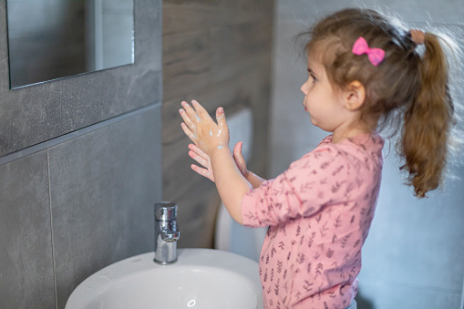 Toddler girl washing her hands with soap and water in modern home bathroom, alone. Learning independence and good hygiene
