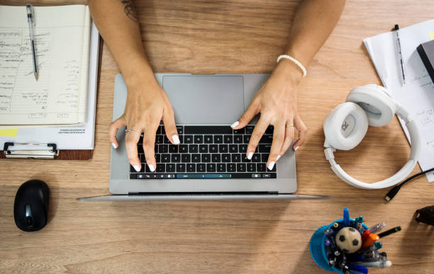 Close-up shot from above of a young woman sitting at a table typing on laptop while working remotely from home