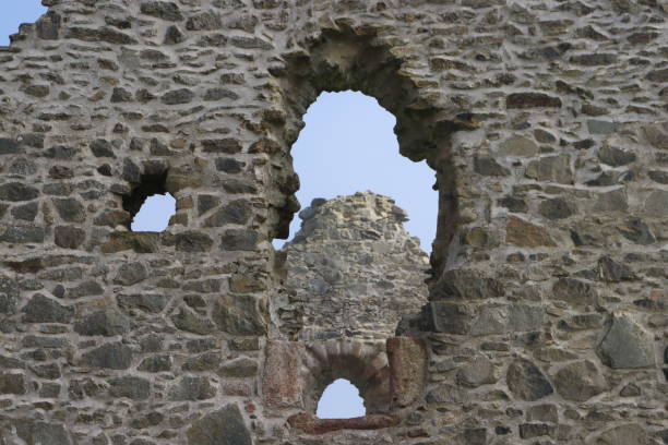 View looking up from the park around the base of the castle to the walls which rise straight from the base of a rocky plateau. Glazed windows are visible in the stone walls. The stone walls are intact and the castle is still inhabited. The medieval castle dates back to Norman times, although the area was first fortified in Celtic times.