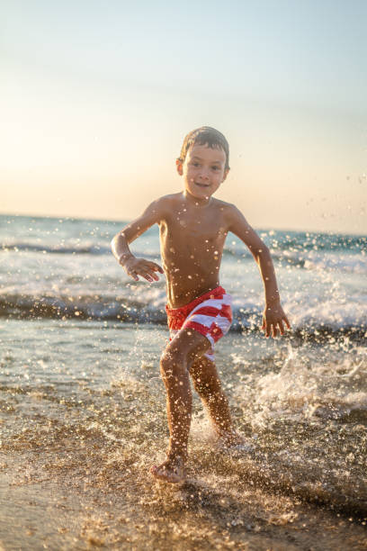 Playful Caucasian boy running into sea and playing with waves, during sea vacation