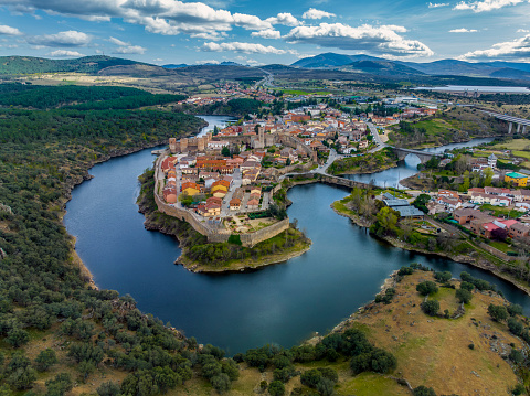 Aerial view of Buitrago del Lozoya, a well preserved historic village near Madrid, surrounded by the Lozoya river, with the Guadarrama mountain chain and reservoir in the background. Long exposure.