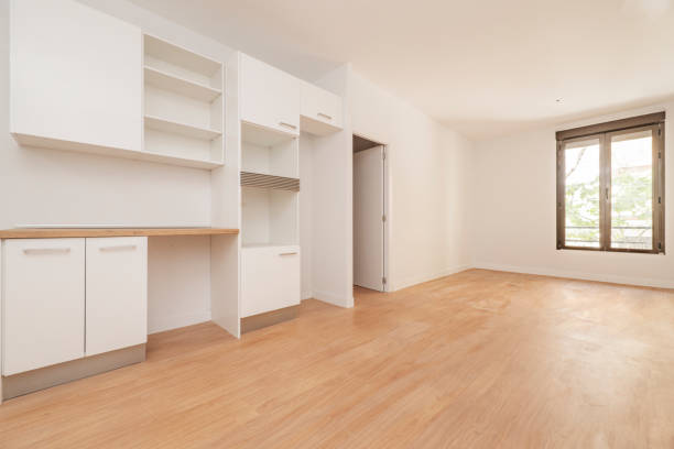 istock Empty living room with kitchen cabinets on one wall, freshly painted walls, light oak floor and bronze colored aluminum window 1484093440