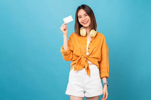 Cheerful beautiful Asian woman holding mockup credit card on blue background.