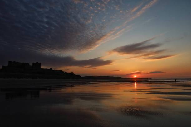 tramonto sulla spiaggia con castello sagomato e paesaggio nuvoloso. - castle bamburgh english culture old foto e immagini stock