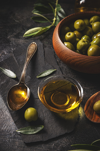 Green olives with olive oil concept on black slate background